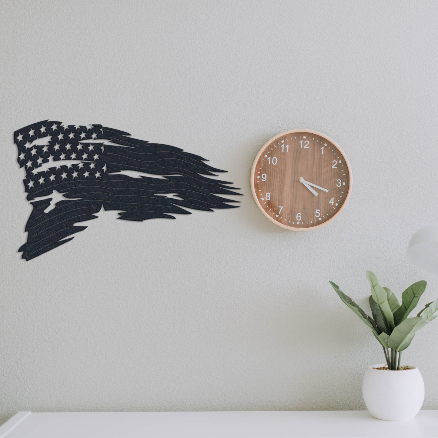 American flag wall metal art on a light gray wall with a wooden clock and plant.