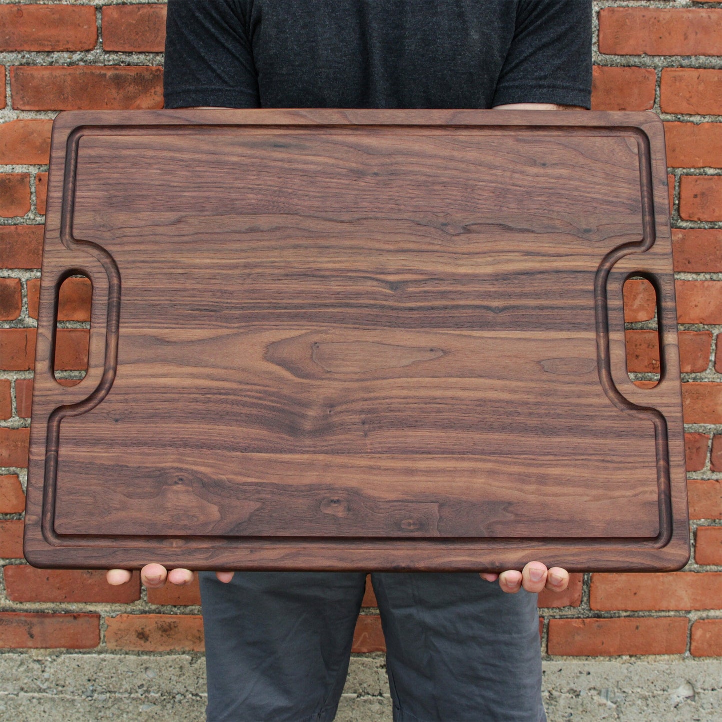 Person holding a wooden cutting board against a brick wall