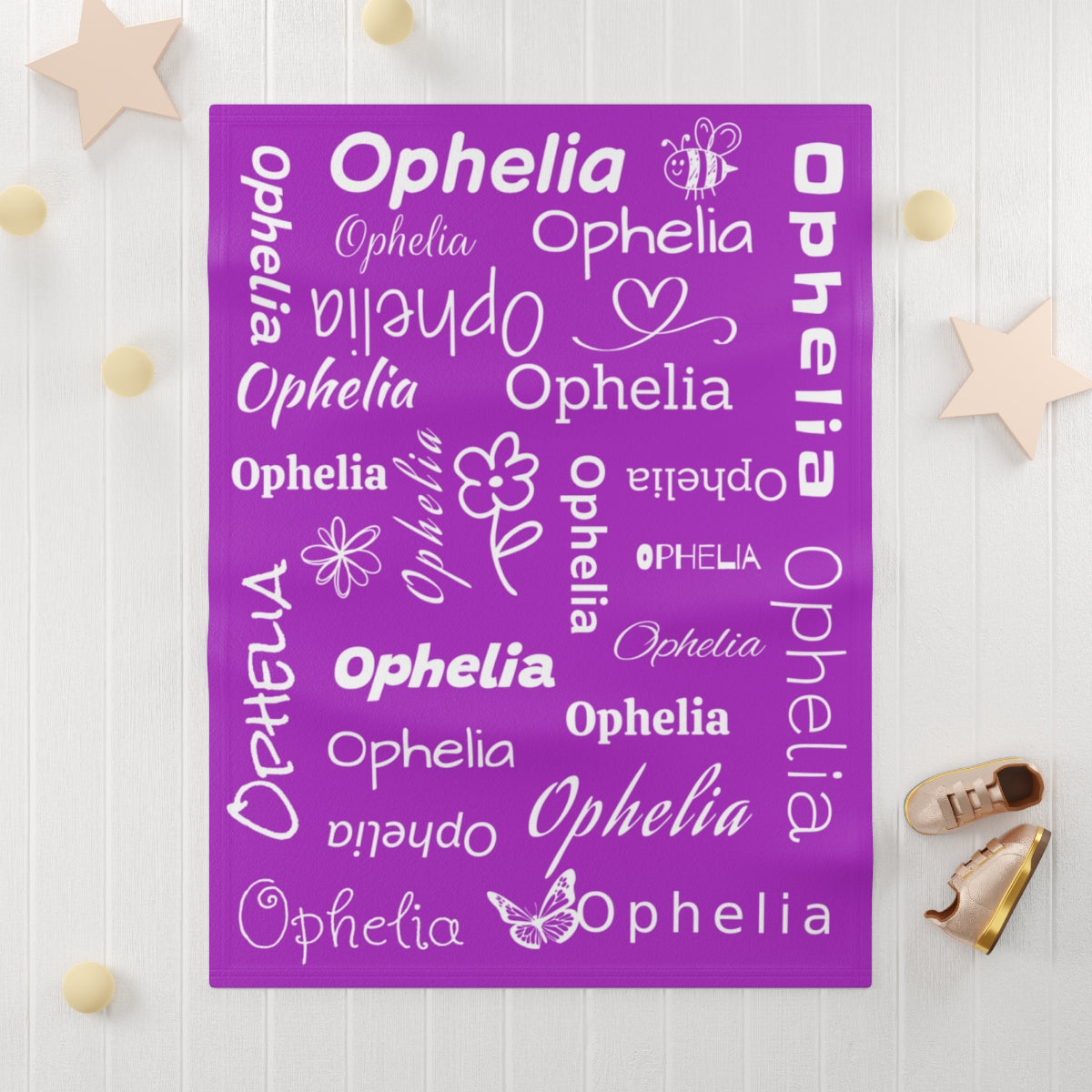 Purple decorative plush blanket with the name 'Ophelia' in various fonts on a white wooden background.