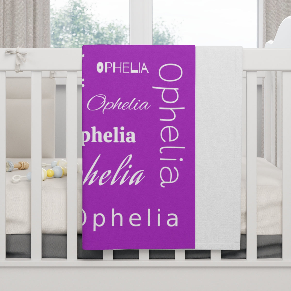 Purple blanket with 'Ophelia' printed repeatedly in various fonts on a white crib.