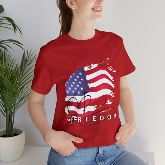 Person wearing a red t-shirt with an American flag and 'FREEDOM' text, standing indoors next to a plant.