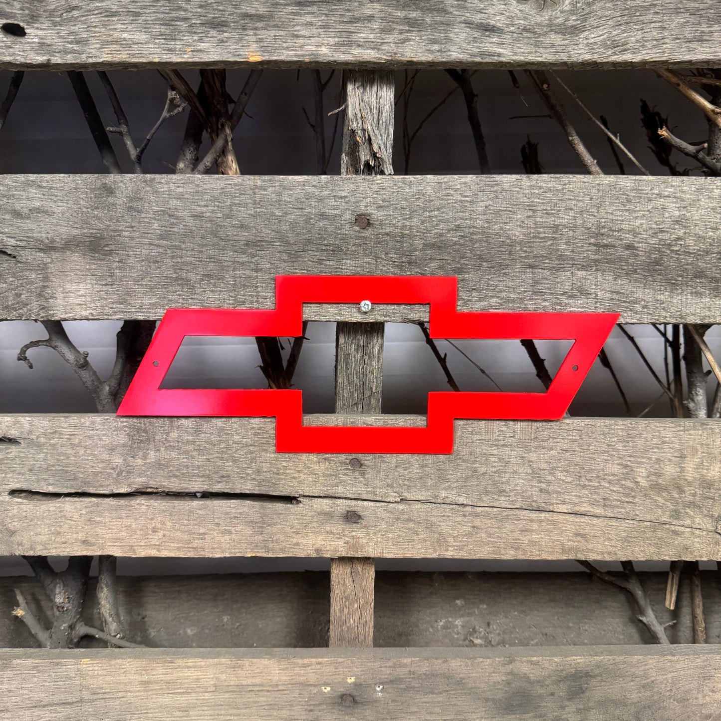Red Chevrolet logo on a wooden surface with a natural background