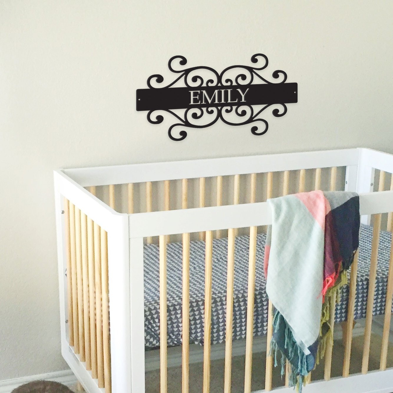 White crib with a decorative nameplate above it in a nursery setting.