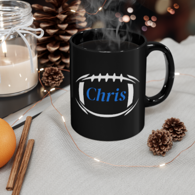 Black mug with 'Chris' design, steaming hot, surrounded by decorative items on a table.