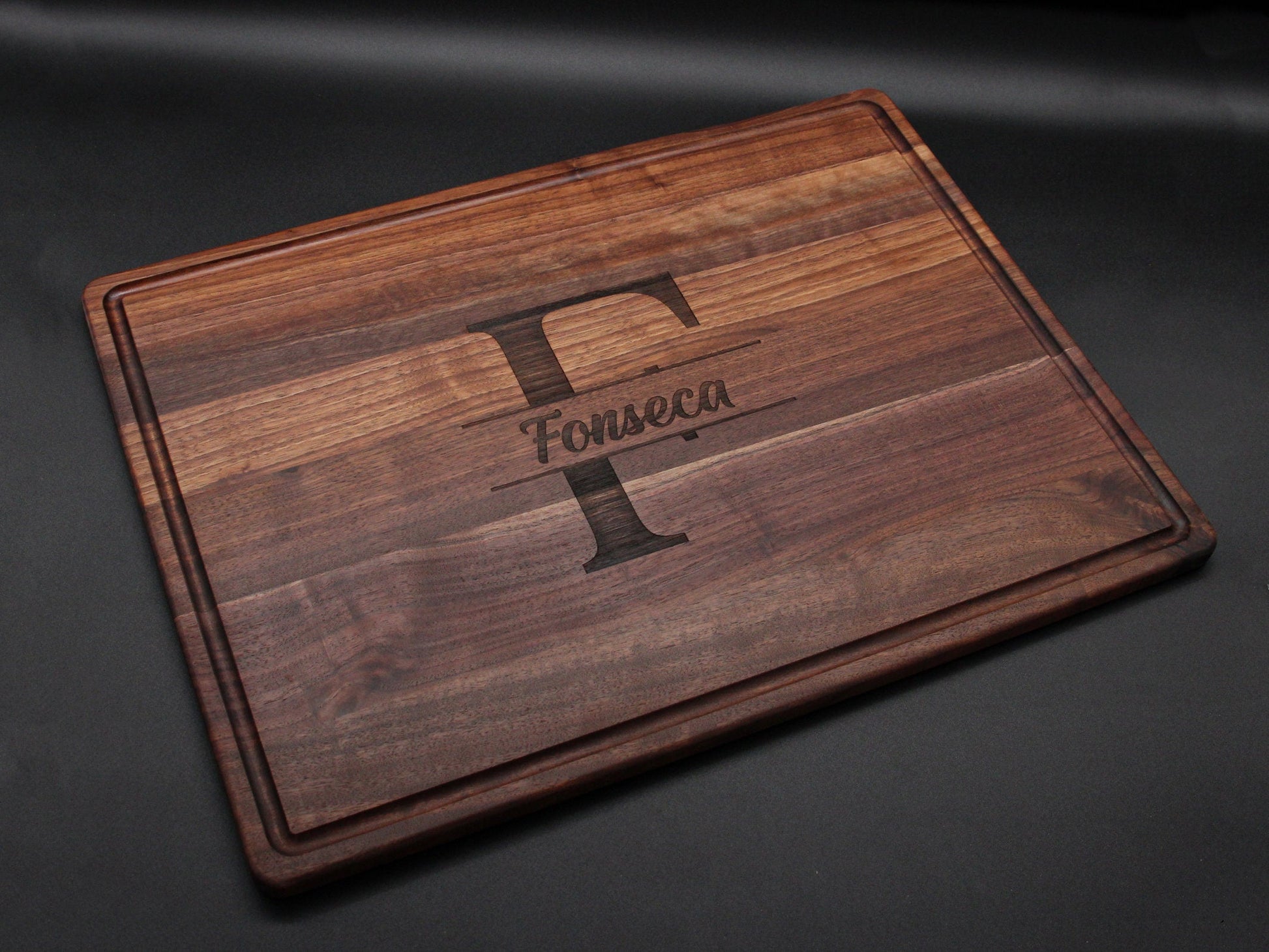 Wooden cutting board with engraved letter 'F' and name 'Fonseca' on a dark background