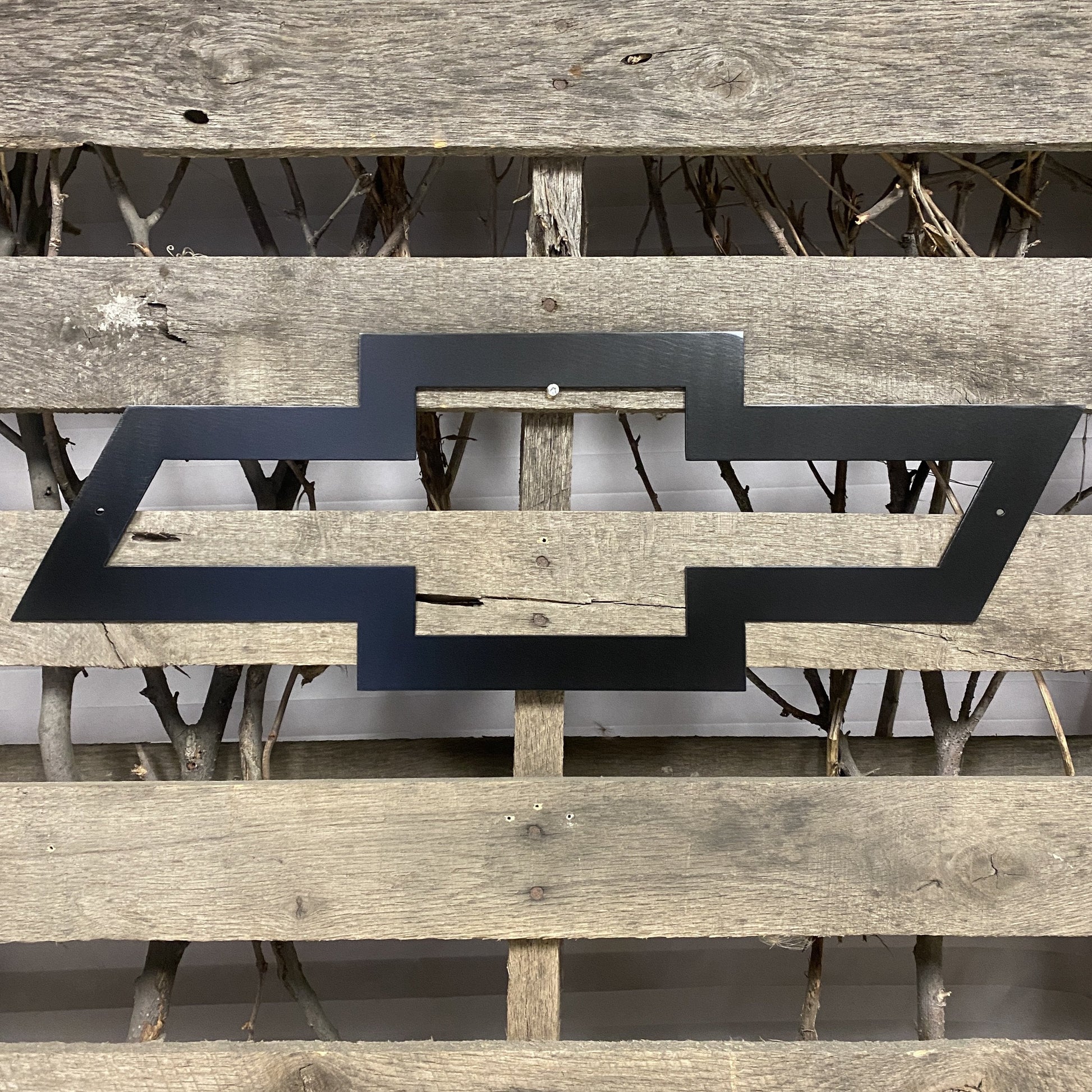 Black Chevrolet logo on a wooden surface with a natural background